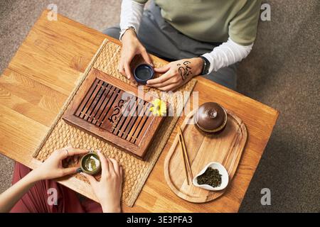 Un giovane adulto asiatico e una giovane donna adulta asiatica seduti a un tavolo di legno che partecipa alla tradizionale cerimonia del tè, che tiene dei tazze da tè e condivide l'esperienza culturale insieme Foto Stock