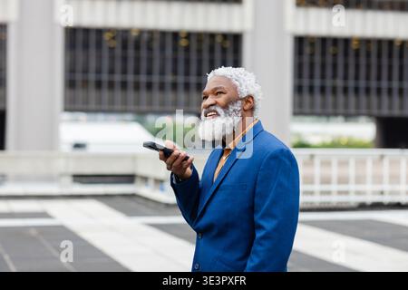 Uomo afroamericano anziano in tuta blu che parla sullo smartphone sulla terrazza sul tetto Foto Stock