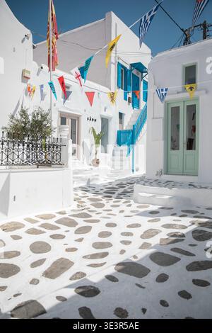 Vista degli edifici bianchi e soleggiati adornati da vivaci accenti blu e colorate stradine acciottolate, Mykonos, Grecia. Foto Stock