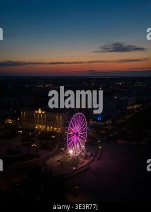 Veduta aerea di una radiosa ruota panoramica che si illumina sul paesaggio urbano al crepuscolo, con una magica tonalità viola sulla scena, Sorrivoli, Emilia Romagna, Foto Stock