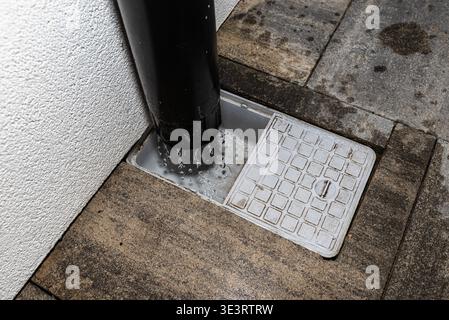L'acqua piovana che scorre da un beccuccio a valle in un bacino di raccolta con una griglia filtrante Foto Stock