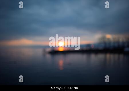 Sfondo volutamente sfocato di un tramonto su un lago calmo con un cielo nuvoloso scuro Foto Stock