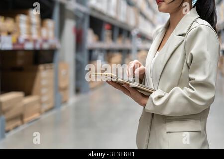 donna asiatica proprietaria di un'azienda che utilizza un tablet digitale controlla la quantità di scorte di prodotti disponibili sullo scaffale presso la fabbrica del magazzino di distribuzione. attività logistica Foto Stock