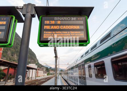 Pannello informativo che mostra i dettagli di un treno in partenza alla stazione ferroviaria di Laveno Mombello, Italia. Tabella degli orari dei trasporti pubblici che mostra il treno tim Foto Stock