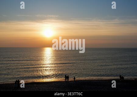 Caldo tramonto sul Mar Baltico con riflessi dorati sulle acque calme e sagome delle persone che si godono la serata sulla spiaggia sabbiosa Foto Stock