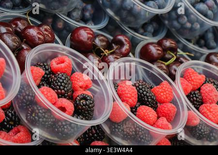 Bacche fresche assortite, tra cui lamponi e more, confezionate in piccoli contenitori di plastica, esposte con ciliegie e mirtilli in un outdoo Foto Stock