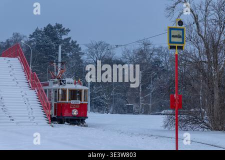 Tram rosso storico che guida su piste innevate accanto a un cartello di fermata del tram in inverno Foto Stock