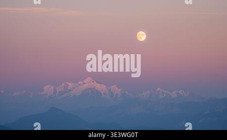 Una vista mozzafiato del Monte bianco illuminata dalla luna piena, che proietta una luce serena sulle cime innevate delle Alpi contro un cielo dalle tonalità pastello Foto Stock