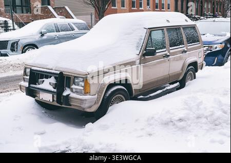 Scena urbana dopo una forte nevicata, con auto sepolte sotto la neve e strade fiancheggiate da strati bianchi incontaminati. Questo paesaggio invernale cattura Foto Stock