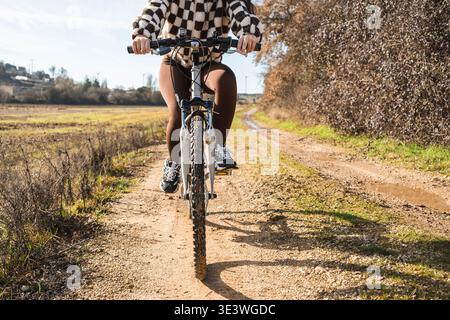 Una donna pedala in mountain bike lungo un sentiero rurale sterrato, godendosi la giornata di sole in un ambiente di campagna. La bicicletta getta un'ombra sul sentiero accidentato Foto Stock