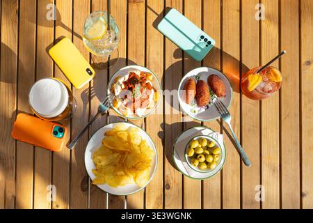 Un vivace assortimento di tradizionali tapas spagnole, con olive, patatine fritte, crocchette e molto altro ancora, disposti su un tavolo di legno accanto al rinfresco Foto Stock