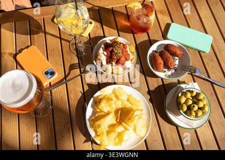 Una vivace varietà di tradizionali tapas spagnole, tra cui olive, crocchette e patatas bravas, accompagnate da bevande rinfrescanti su una rustica ta di legno Foto Stock