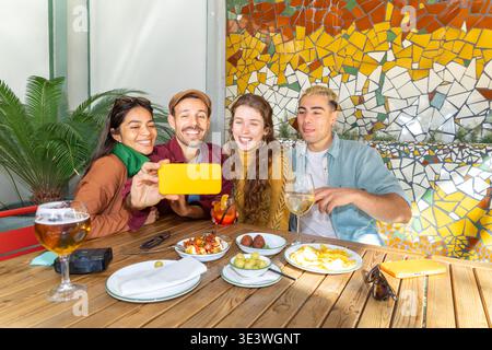 Un gruppo di amici si diverte a divertirsi, ridere e scattare selfie mentre condividono deliziose tapas. La loro connessione e autenticità risplendono durante la Foto Stock