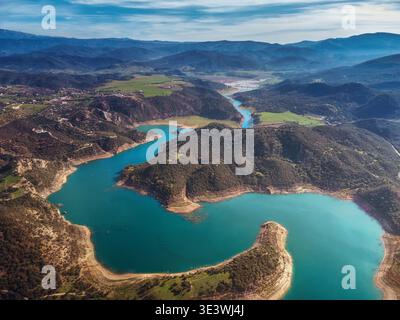 Scatto aereo che cattura un tranquillo fiume blu che si snoda tra lussureggianti colline e valli verdi, mostrando la bellezza della natura e la tranquillità del sc Foto Stock