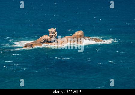 Una vista panoramica di un aspro affioramento roccioso nelle acque azzurre del mare al largo della costa delle Asturie. La consistenza ruvida contrasta con le onde lisce dell'oceano, SY Foto Stock