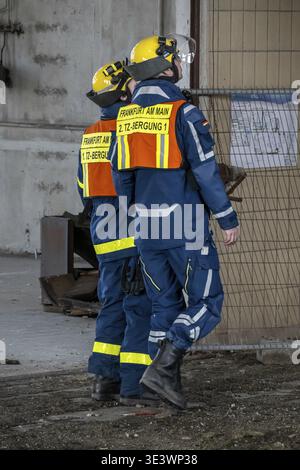 Due lavoratori THW con indumenti protettivi attraversano un edificio industriale indossando giubbotti di sicurezza Foto Stock