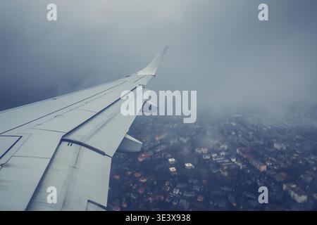 Airplane Wing Over City Aerial View durante Cloudy Approach Landing Over Urban Neighborhood Foto Stock