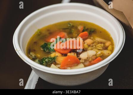 Un piatto di carta di zuppa di verdure fatta in casa con carote, verdure e fagioli, servito caldo in una semplice ciotola bianca, che evoca comfort e una sana alimentazione Foto Stock