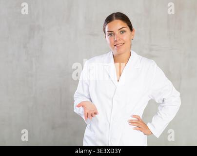 Dottore in camice bianco sorridente alla macchina fotografica mentre si presenta con la mano e punta con il dito Foto Stock