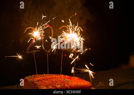 Torta festosa decorata con spruzzette colorate e scintillanti che formano l'anno 2026 brillanti su uno sfondo scuro. Foto Stock