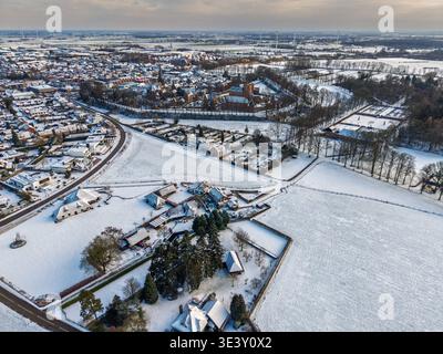Vista aerea panoramica di una città europea innevata con il castello di Huis Bergh. Un paesaggio invernale panoramico con campi ghiacciati, case residenziali e vinci Foto Stock