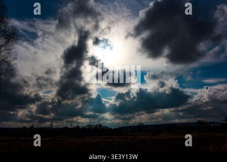 I potenti raggi del sole penetrano attraverso un'imponente arazzo di nuvole di tempesta buie e pesanti. Un cielo moodo sopra una terra dalla silhouette sagomata Foto Stock