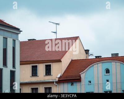 I tetti color pastello si innalzano sotto un cielo morbido e nuvoloso. Le piastrelle rosse contrastano con le facciate color crema e blu. Le antenne si aprono in cima a tranquilli edifici in stile europeo. Foto Stock