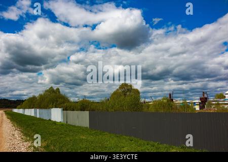 Il cielo nuvoloso si staglia su un vergine erboso e una lunga recinzione che confina con un sito industriale Foto Stock