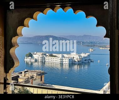 Il Palazzo del Lago Taj nel Lago Pichola è incorniciato da una finestra ad arco nel Palazzo cittadino di Udaipur. Foto Stock