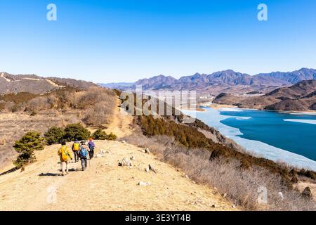 Paesaggio montano panoramico vicino a Pechino, Cina, con colline ondulate, un bacino idrico blu, sinuosi rigogliosi, vegetazione invernale secca Foto Stock