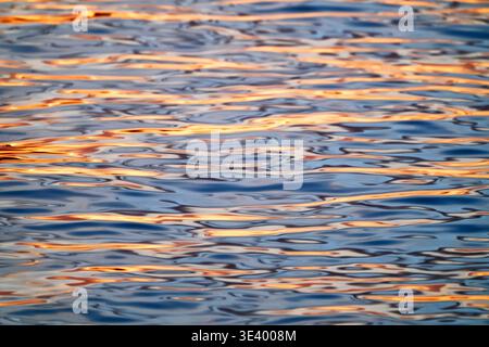 Consistenza astratta dell'acqua di mare con riflessi dorati del tramonto sulla superficie ondulata, Varigotti, Liguria, Italia. Foto Stock