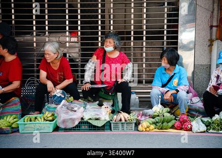 Contea di Hsinchu, Taiwan - 21 luglio 2023: I venditori di donne anziane si siedono su un marciapiede che vende frutta e verdura fresca davanti a un otturatore metallico. Foto Stock