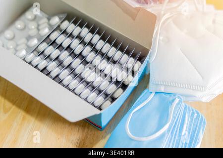 Una grande quantità di maschere mediche si trovano accanto a una pila di pillole su una scatola per l'inizio del trattamento. Medicina e assistenza sanitaria. Foto Stock