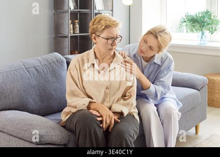 La madre e la figlia adulta, seduto sul divano di casa, offrono comfort e cura Foto Stock
