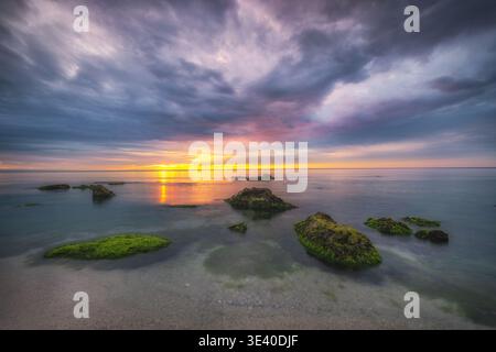 Bellissimo paesaggio nuvoloso sulle onde del mare e sul paesaggio roccioso della spiaggia all'alba Foto Stock