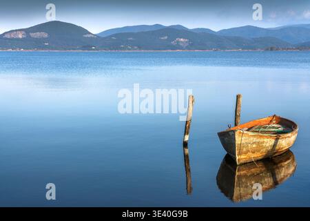 Vista di un'antica barca in legno ormeggiata sul Lago Massaciuccoli a Torre del Lago. Acque blu calme con riflessi e colline sullo sfondo, Versilia, Luc Foto Stock