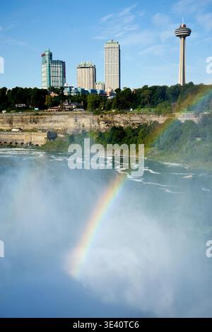 Un vivace arcobaleno attraversa la nebbia delle Cascate del Niagara, Ontario, Canada, con la Skylon Tower e lo skyline della città sullo sfondo. Foto Stock