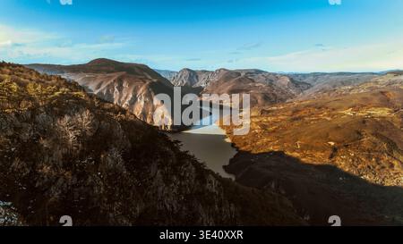 Vista aerea del fiume Drina che si snoda attraverso un aspro paesaggio di canyon, con luci e ombre contrastanti che evidenziano le texture della montagna Foto Stock