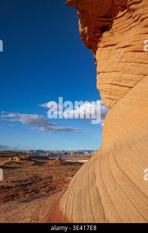 Formazione di roccia arenaria curva che si affaccia sul terreno desertico con mesa lontane e cielo blu con nuvole sparse in un paesaggio arido Foto Stock