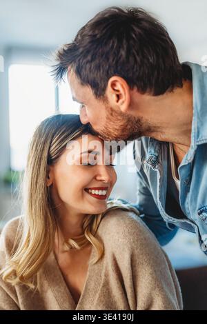 Coppia felice e variegata che condivide un momento di gioia a casa, abbracciando e sorridendo insieme Foto Stock
