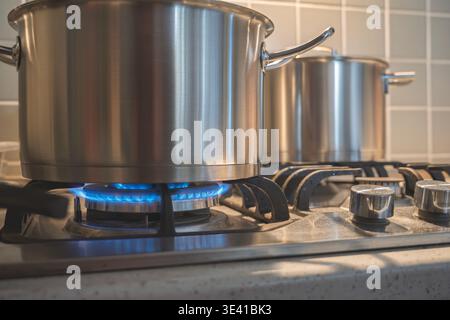 Primo piano di pentole metalliche che bollono su un fornello a gas illuminato in una moderna cucina di casa piastrellata Foto Stock