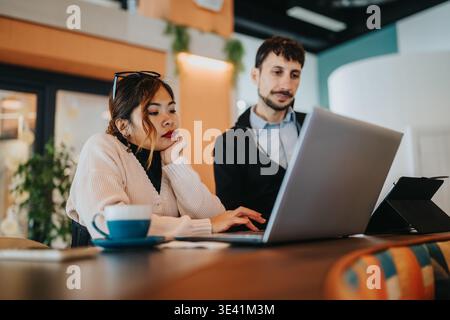 Lavoratori aziendali che collaborano con un notebook in un moderno bar di coworking, concentrati sulle attività di progetto Foto Stock