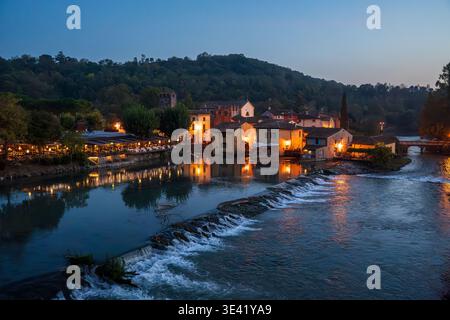 Suggestiva vista notturna di Borghetto sul Mincio, uno dei borghi più belli d'Italia. L'immagine cattura le case illuminate riflesse nel Mincio Ri Foto Stock