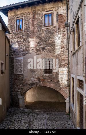 Suggestiva vista su un vicolo storico di Feltre, Belluno. L'immagine mostra un imponente edificio in pietra e mattoni con un grande arco sopra il tradizionale cobb Foto Stock