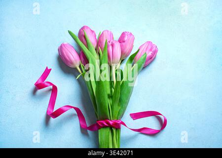 Tulipani rosa su sfondo blu pastello. Mockup floreale primaverile per biglietti d'auguri o invito. Delicato mazzo di fiori di tulipano con nastro. Foto Stock