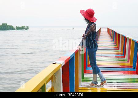 Donna con cappello rosso che guarda il mare dal colorato lungomare di legno Foto Stock