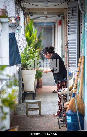 La donna lava i piatti in vicoli stretti. Corridoio della linea di piante. Indossa pantaloni a motivi geometrici e camicia nera. La luce solare mette in risalto le piastrelle bagnate Perfetto per Our Foto Stock