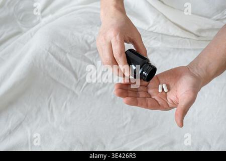 Uomo irriconoscibile che versa capsule bianche pillole a portata di mano dal barattolo, fondo bianco del letto, spazio di copia. Paziente che prende la medicina, l'autoterapia, l'auto sanitaria Foto Stock