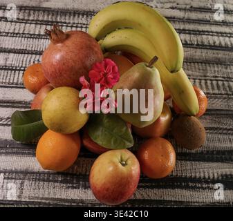 Vari frutti sono disposti in un mucchio, con un fiore rosso in cima ai frutti. Foto Stock