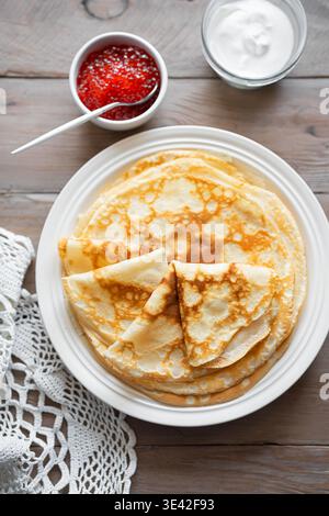 Crepes sottili fatte in casa con caviale rosso e crema su sfondo di legno, vista dall'alto. Pancake salati con caviale di pesce salmone. Traditore della settimana dei pancake di Maslenitsa Foto Stock